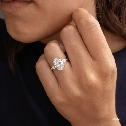 Detalle de anillo de compromiso oval three-stone 3.00 ct con diamantes laterales y engaste en oro.