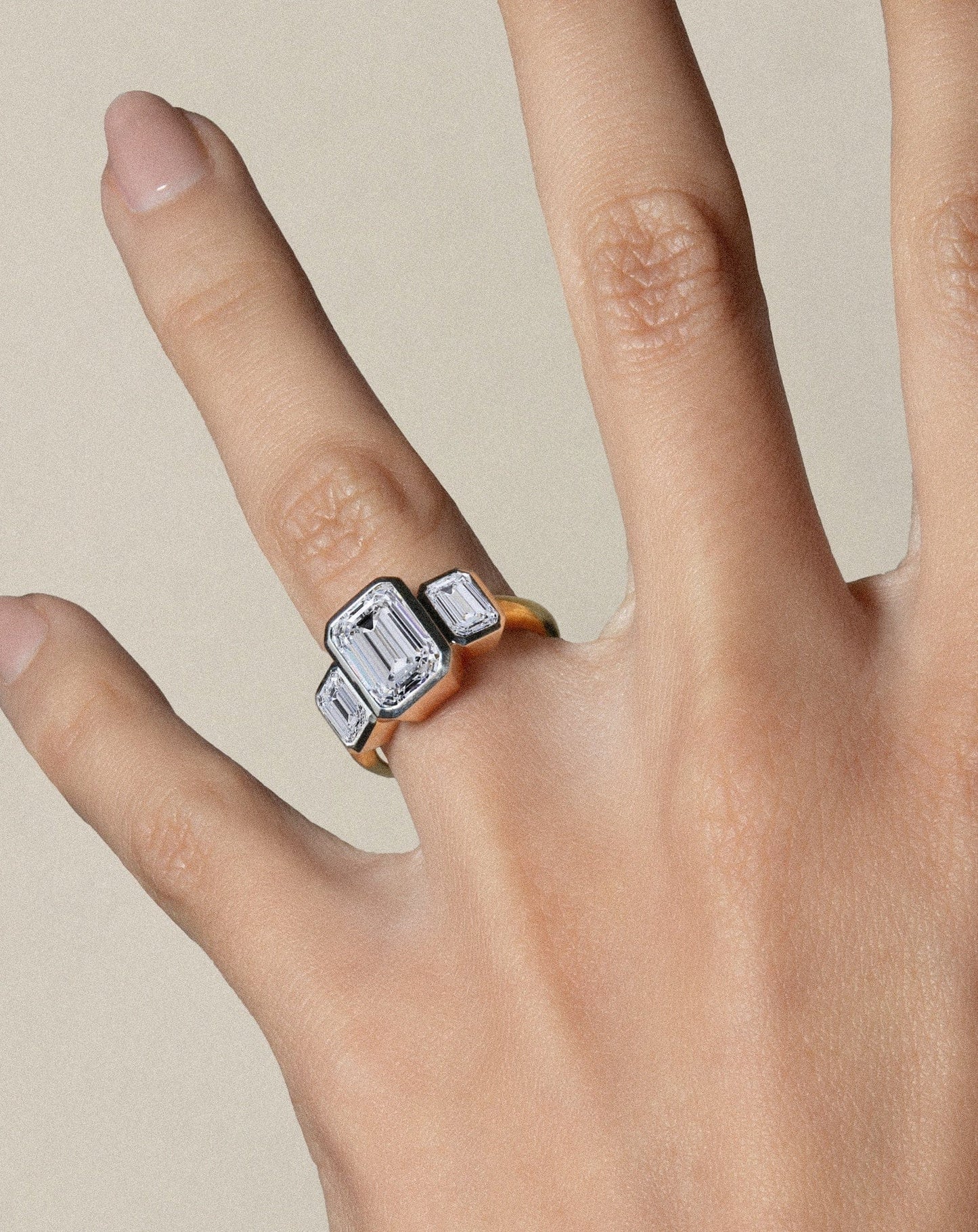 Detalle de anillo three-stone emerald con bisel en oro, diseño moderno y estructurado.