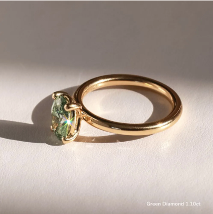 Detalle de diamante verde oval 1.10 ct en anillo de compromiso minimalista, montura solitario de cuatro garras en oro.