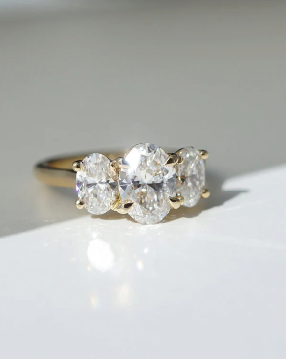 Anillo de compromiso con diamantes de laboratorio corte oval, centro de 1.50 ct y dos piedras laterales de 0.70 ct en oro.