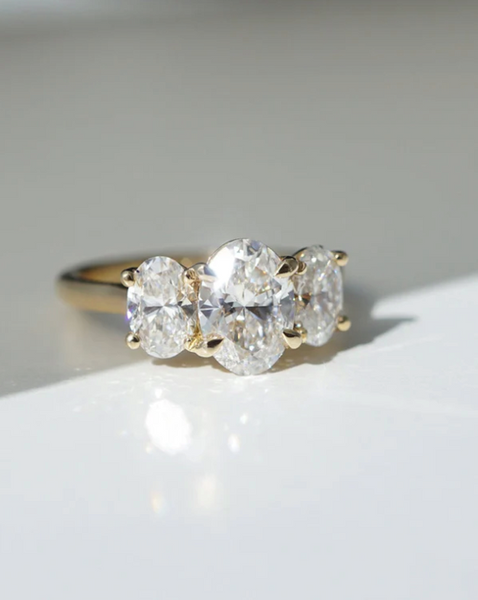 Anillo de compromiso con diamantes de laboratorio corte oval, centro de 1.50 ct y dos piedras laterales de 0.70 ct en oro.