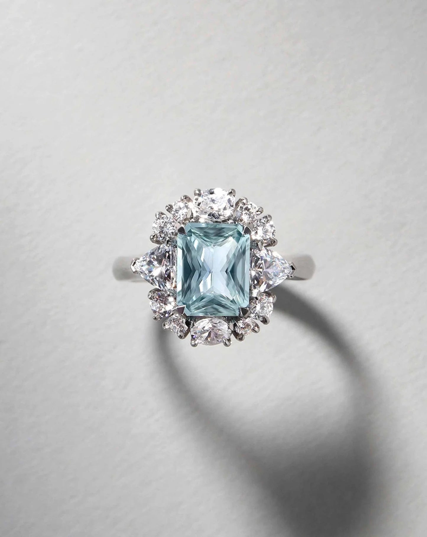 Detalle de anillo fancy azul radiant 2 ct con halo y diamantes laterales en oro.