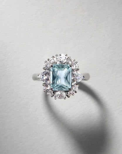 Detalle de anillo fancy azul radiant 2 ct con halo y diamantes laterales en oro.
