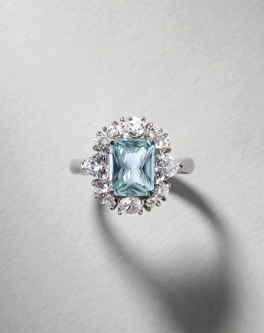 Detalle de anillo fancy azul radiant 2 ct con halo y diamantes laterales en oro.
